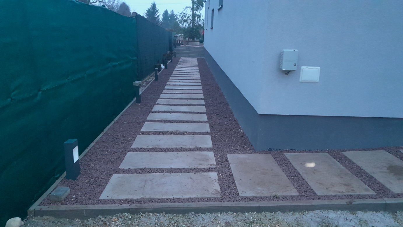Pohľad na vybudovaný chodník. Jedna tvárnica má hmotnosť 95 kg. Klient sa rozhodol, že ich nechce uložiť vedľa seba, ale ako šlapajové kamene. Pred budovaním chodníka sme postavili oplastovaný pletený plot s nepriehľadnou krytinou.