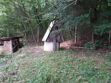 Odkrytá studňa so skladom stavebného materiálu, ktoré boli skryté v húštine náletových drevín a zeliny.